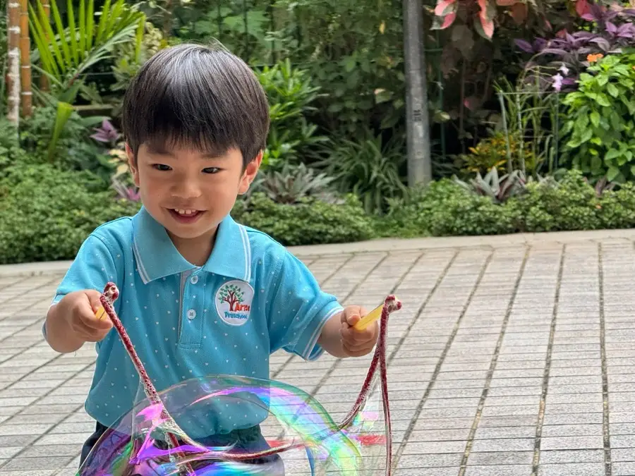 A child making a giant bubble outdoors at Arise Preschool
