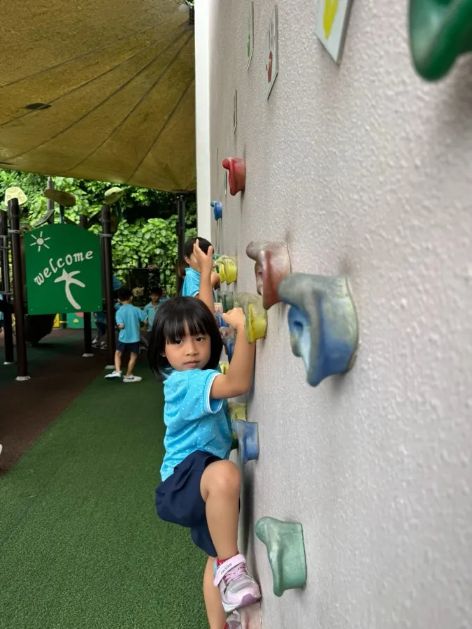 A child climbing the outdoor playground wall at Arise Preschool